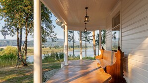 A covered porch with wooden benches, white columns, and a view of a lake and mountains.
