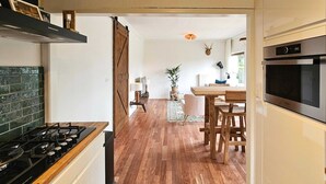 A kitchen with a wooden floor, a stove, and a refrigerator. There is a dining area with a table and chairs.