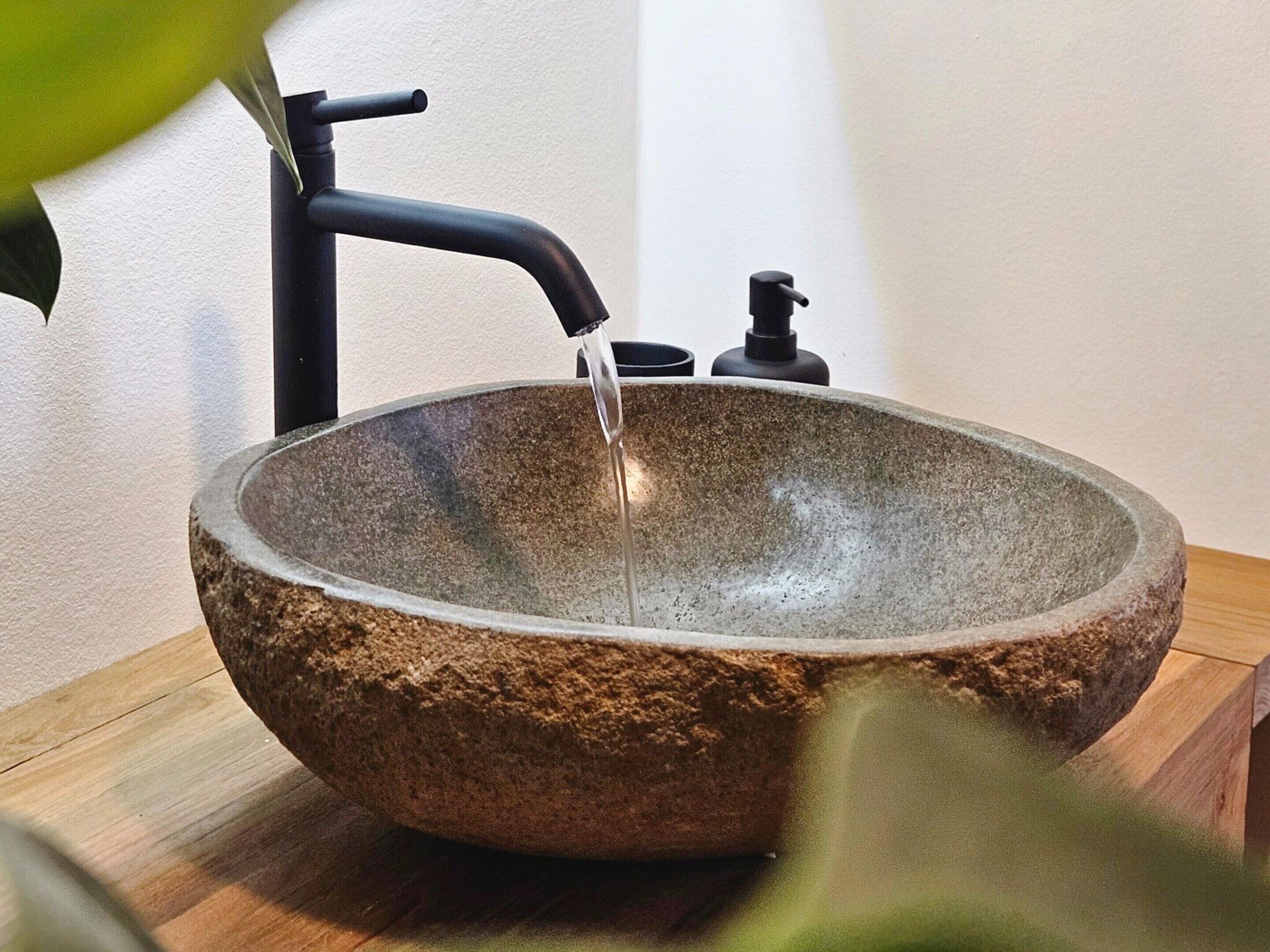 Ein Waschbecken aus Stein mit einem schwarzen Wasserhahn und Seifenspender.