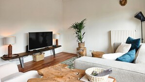 A modern living room with a flat-screen TV, wooden coffee table, and a grey sofa with blue cushions.