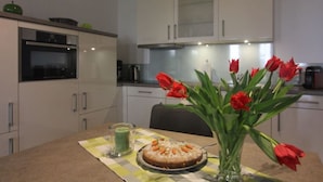 Een moderne keuken met witte kasten, een eettafel met een geruit tafelkleed, een taart en een vaas rode tulpen.