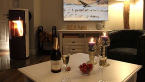 A cozy living room with a fireplace, a television displaying a bird, and a table set with wine glasses and strawberries. - Salt air Comfortable Holiday Residence (Zingst)