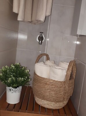 A bathroom with a wooden bench, a woven basket with towels, a potted plant, and a towel rack. - Holiday Apartment Meerzeit (Brodersby)