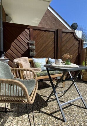 An outdoor patio with wicker furniture, a table, and a brick wall. - Holiday Apartment Meerzeit (Brodersby)