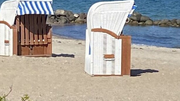 Two beach chairs with striped towels, positioned on a sandy beach with a rocky shoreline and the ocean in the background. - Holiday Apartment Meerzeit (Brodersby)