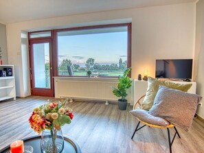 A modern living room with a large window, a television, and a comfortable seating area. - Sea-with-a-view (Neustadt in Holstein)
