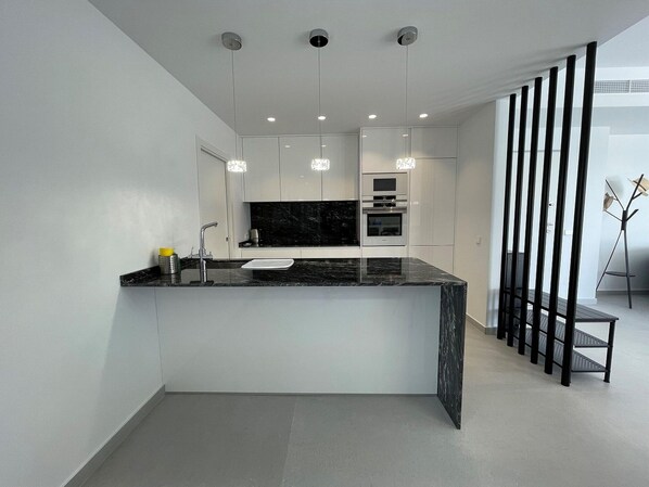 A modern kitchen with a black marble countertop, stainless steel appliances, and pendant lighting. - Modern Villa Near Guardamar (Rojales)