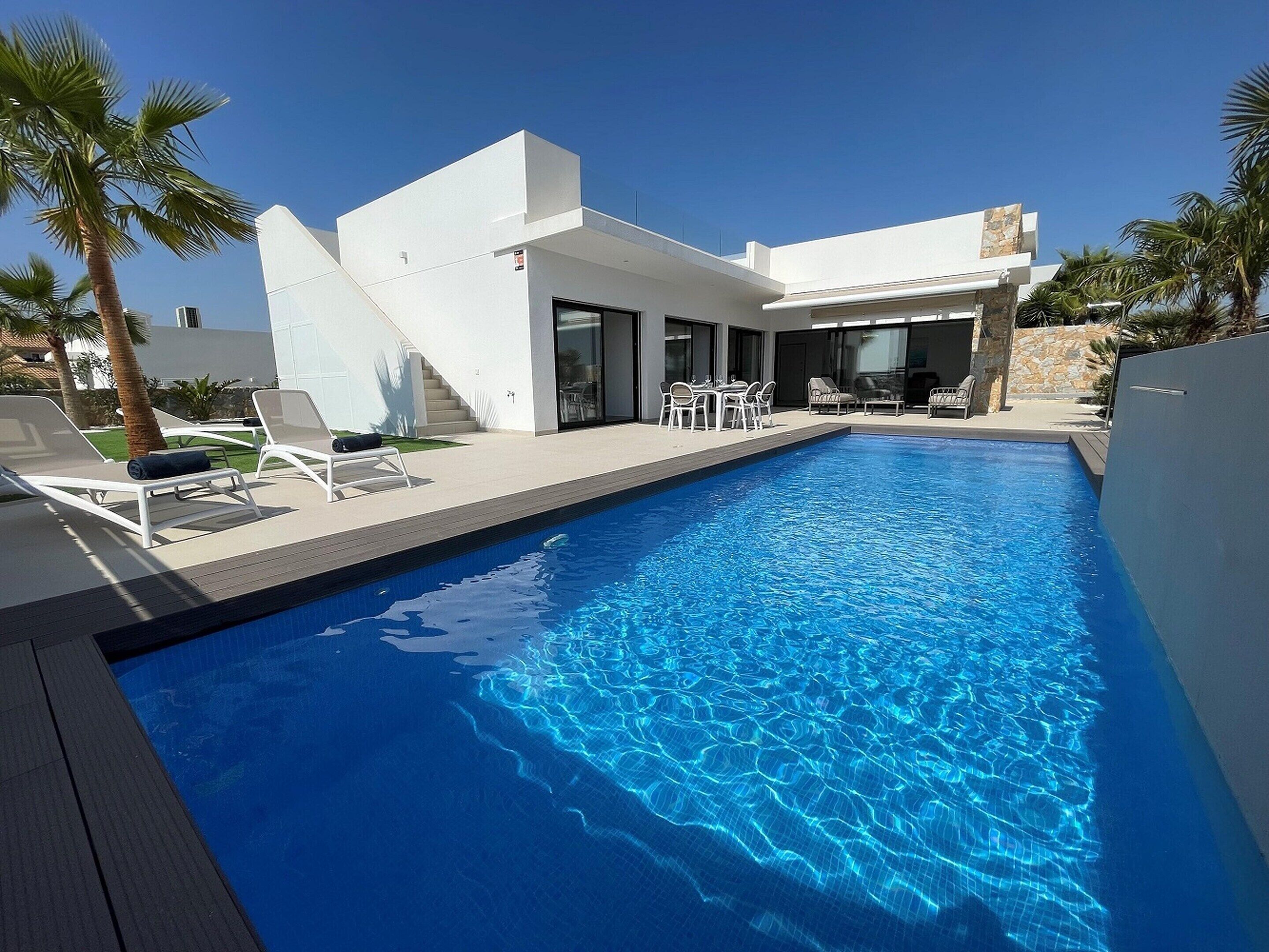 Una casa moderna amb piscina, mobiliari d'exterior i palmeres.