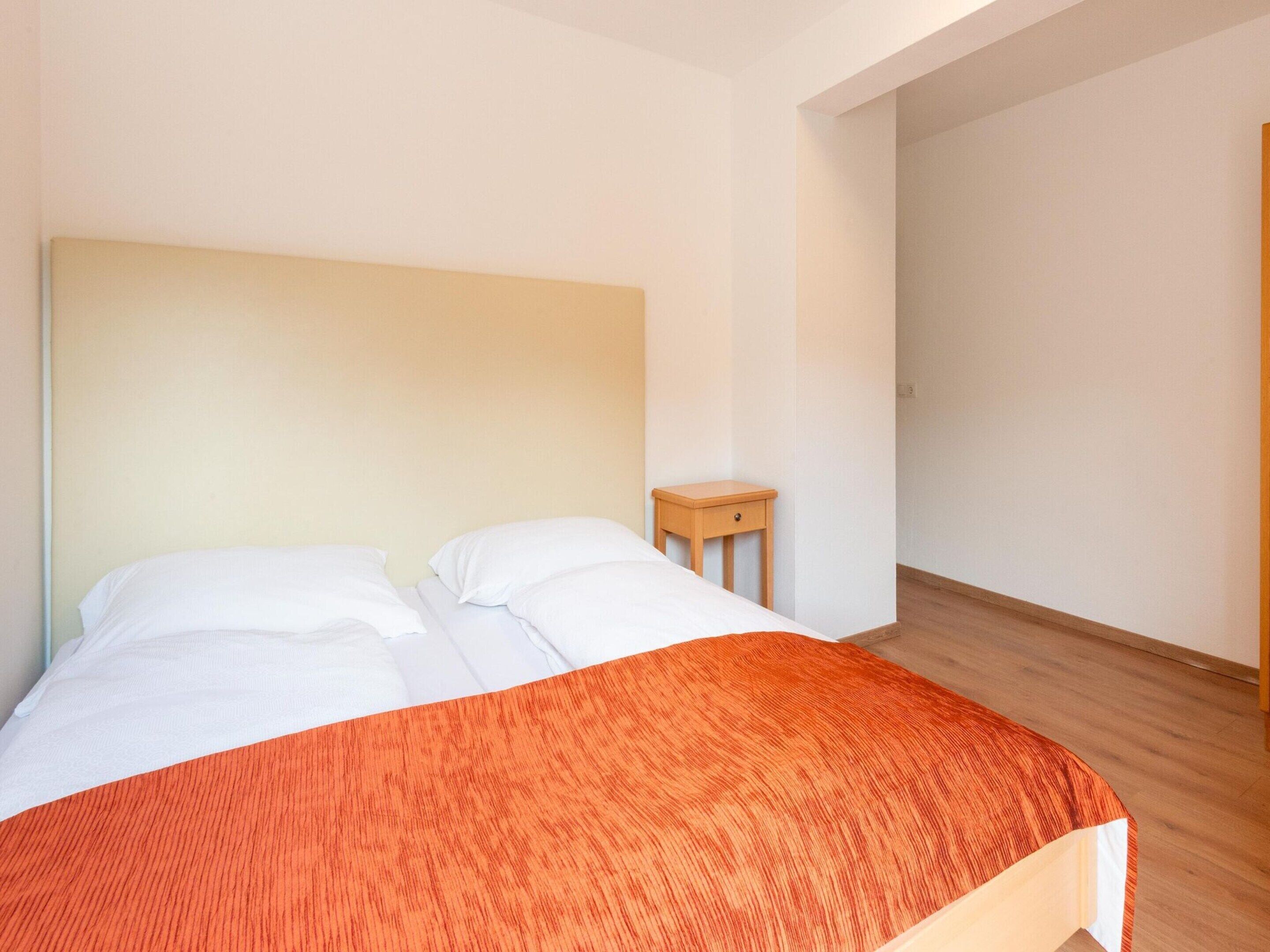 A bedroom with a bed, a small wooden nightstand, and a plain wall.
