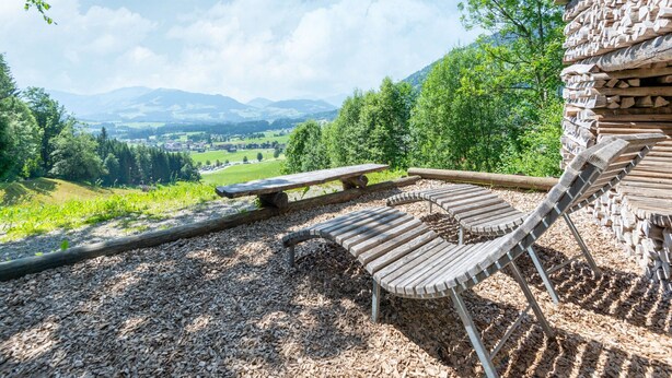Una terraza de madera con un banco y una mesa de picnic con vistas a un paisaje pintoresco con montañas y árboles.