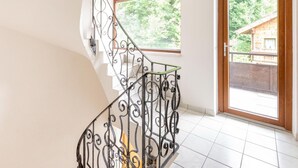 Una escalera con barandillas metálicas ornamentales y vista a una cabaña de madera a través de una puerta de cristal.