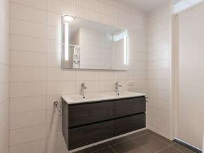 A modern bathroom with a white tiled wall, a large mirror, a double sink, and dark wood cabinetry. - Modern Apartment With Harbour View in Kamperland (Kamperland)