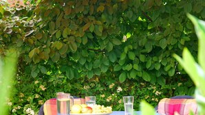 An outdoor dining area with a table set for two, surrounded by lush greenery. - Holiday Apartment With Castle View (Wernigerode)