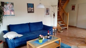 A living room with a blue sofa, a glass coffee table, a potted plant, and a bottle of wine. - Holiday Apartment With Castle View (Wernigerode)