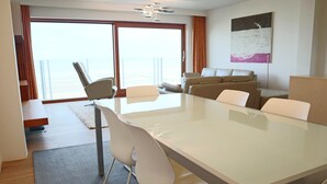 A modern hotel room with a large glass table, comfortable seating, a sofa, and a view of the sea through large windows. - Apartment in Nieuwpoort Near the Marina (Nieuwpoort)
