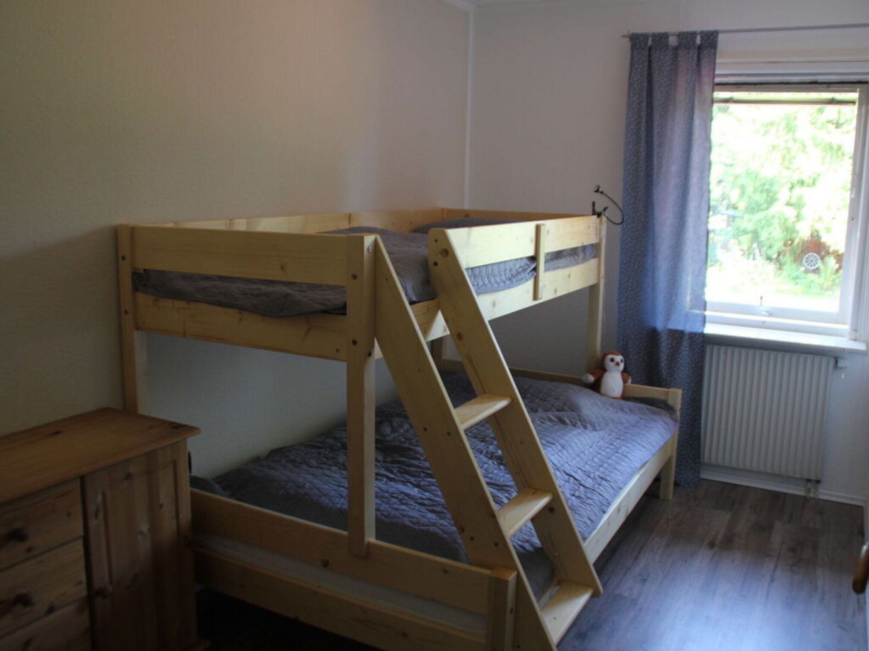 Habitación con literas, una escalera de madera, una mesita de noche pequeña y una ventana con cortinas.
