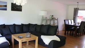 A living room with a dark-colored sofa, a wooden coffee table, and a dining area with a table and chairs. - Nyhyttan Comfortable Holiday Residence (Nora)