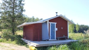 A small, single-story cabin with a red exterior and a gray door, situated in a grassy area with trees in the background. - Nyhyttan Comfortable Holiday Residence (Nora)
