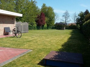 Une pelouse bien entretenue avec un banc en bois et un vélo, un bâtiment en briques et un kiosque en arrière-plan.