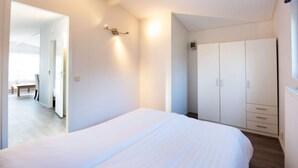 A bedroom with a large bed, a wardrobe, and a small table with chairs. - Holiday Home Chalet Drenthe (Zorgvlied)