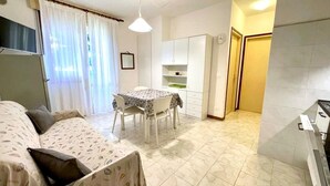 A compact living space with a bed, a dining table, and a kitchenette. - Apartment in Caorle Near the Beach (Caorle)