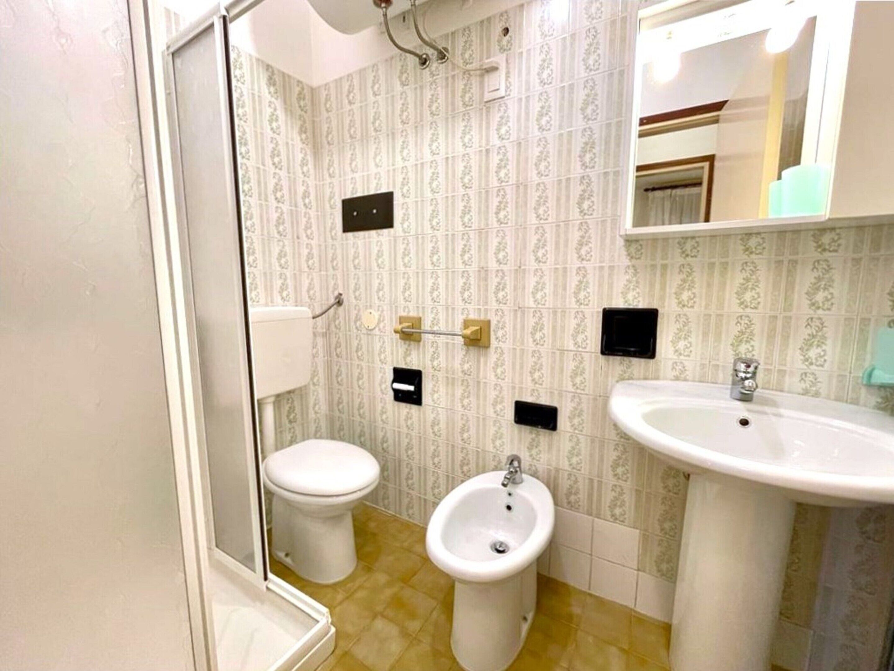 A bathroom with a toilet, bidet, and sink, featuring patterned wallpaper and a mirror above the sink.