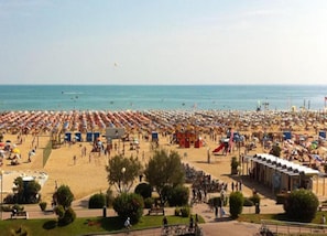 A beach with rows of umbrellas and beach chairs, a playground, and a few people walking. - Apartment in Caorle Near the Beach (Caorle)