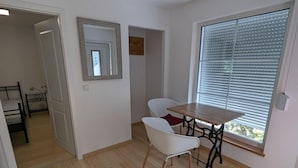 A room with a wooden floor, a dining table with two chairs, a window with blinds, and a mirror on the wall. - Holiday Home Werder/havel (Werder (Havel))