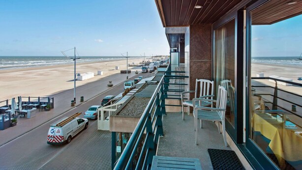 A balcony with a view of the beach and ocean, featuring outdoor seating and a view of the street below. - Royal 201 Seafront Apartment in a top Location (Koksijde)