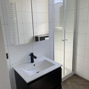 A bathroom with a white sink, black cabinet, and a glass shower enclosure. - Modern Chalet With a Dishwasher in Lathum (Lathum)