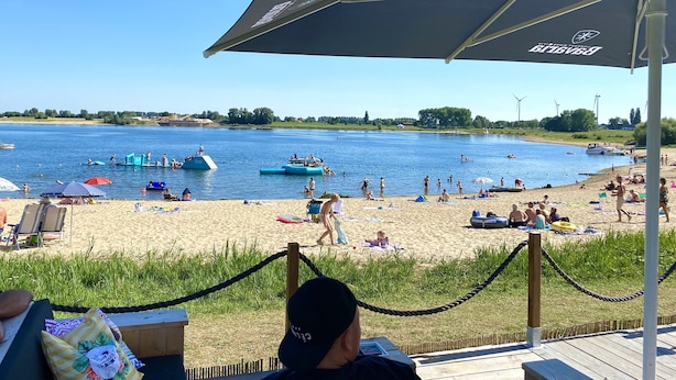 Una playa con una terraza de madera, sillas de descanso y sombrillas.