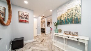 Un pasillo con piso de madera, una consola blanca con cajones, un espejo y arte en la pared, incluyendo un letrero que dice 'Live Music' y otro que dice 'Dream'.