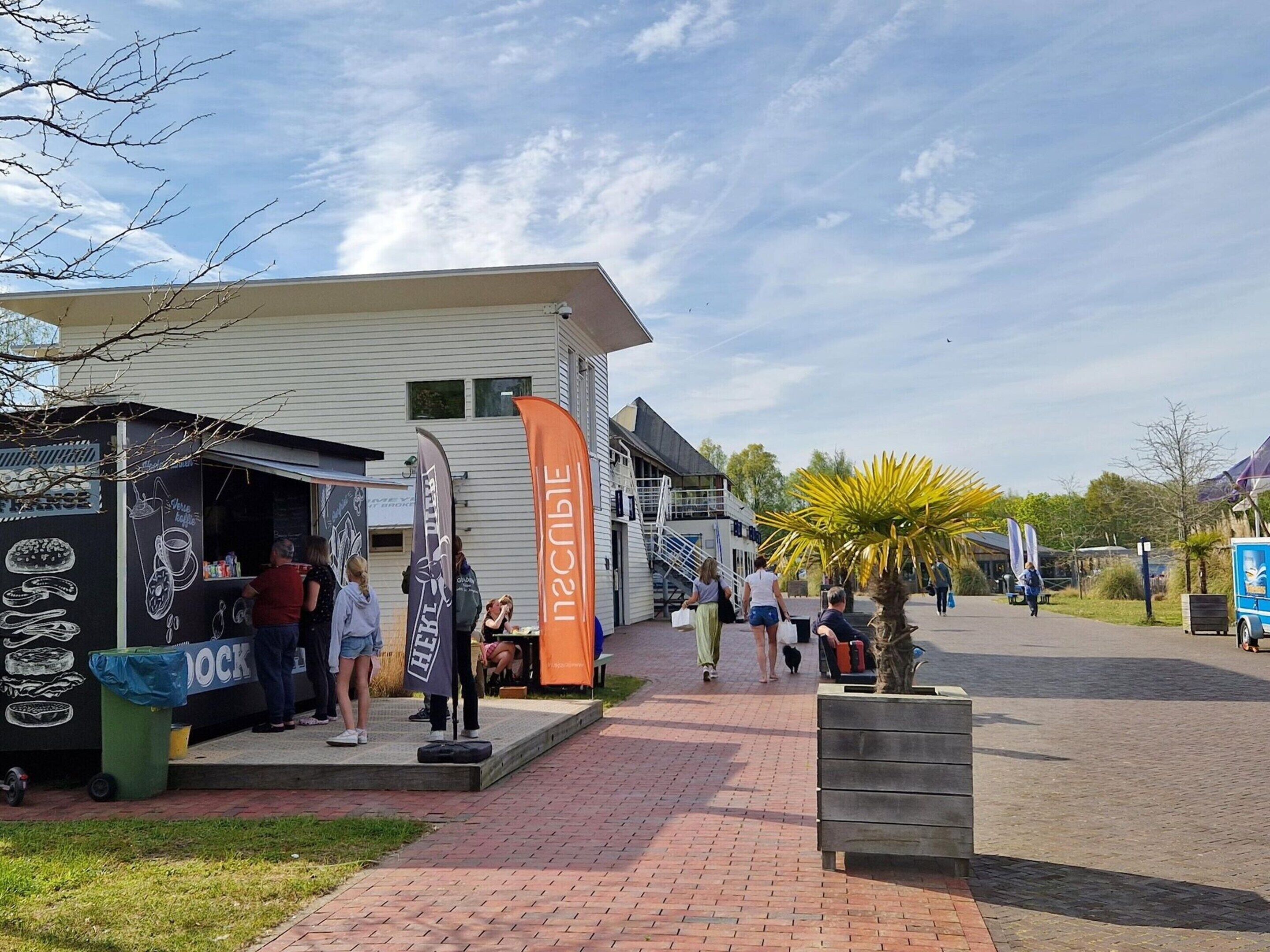 A brick-paved outdoor area with a food stall, a building with a staircase, and a palm tree.