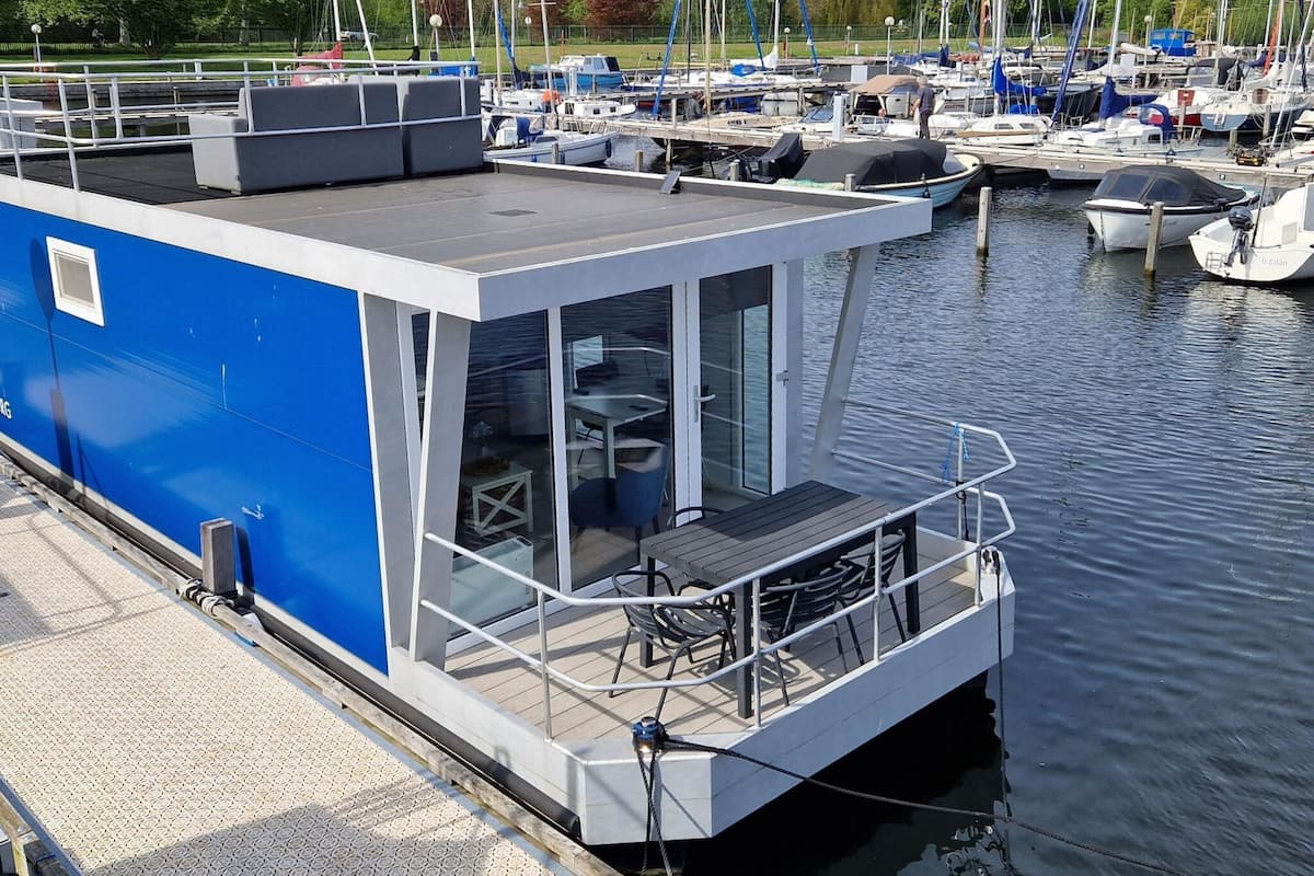 A modern floating structure with a covered deck area, a seating area with tables and chairs, and a glass enclosure.