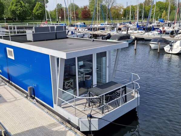 A modern floating structure with a covered deck area, a seating area with tables and chairs, and a glass enclosure. - Water View Lodge in Naarden (Naarden)