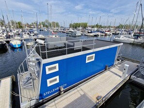 A blue boat named 'STELLENBOSCH' docked at a marina with other boats, a covered deck, and a wooden walkway. - Water View Lodge in Naarden (Naarden)