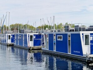 A row of blue and white floating structures with "JOHANNESBURG" and "KAAPSTAD" signage, docked in calm water with boats in the background. - Water View Lodge in Naarden (Naarden)
