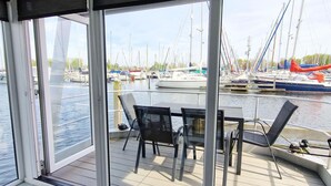 Vue depuis le pont d’un bateau, avec une table et des chaises, donnant sur une marina où sont amarrés différents types de bateaux.