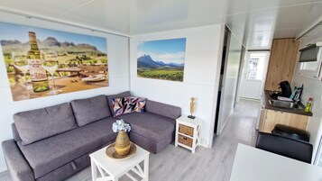 Un espacio habitable moderno con un sofá gris, una pequeña mesa blanca con un florero y dos cuadros con paisajes.