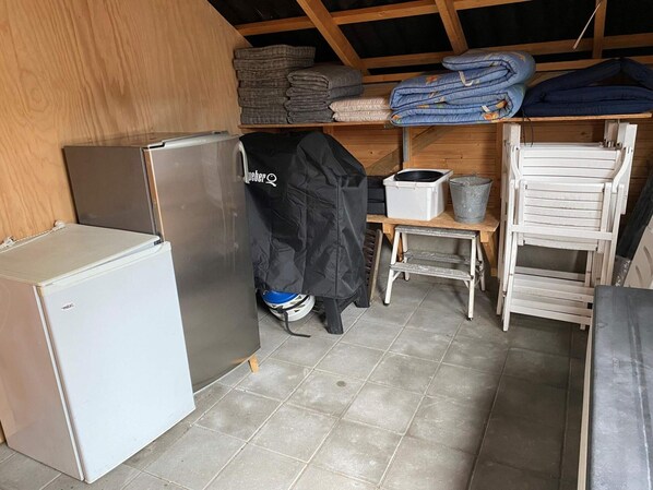 A compact kitchen with a refrigerator, a stove, and a sink. There are shelves with folded blankets and a bucket.