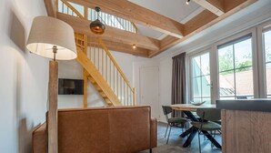 A modern interior with a wooden staircase, a sofa, a dining table with chairs, and large windows. - Luxury new Apartment on Ameland (Buren)
