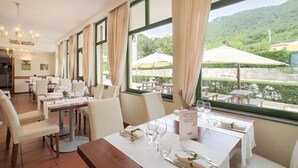 A restaurant with tables set for dining, large windows with curtains, and a view of a lake and greenery. - Apartment in Umbria With Pool and Sauna (Foligno)