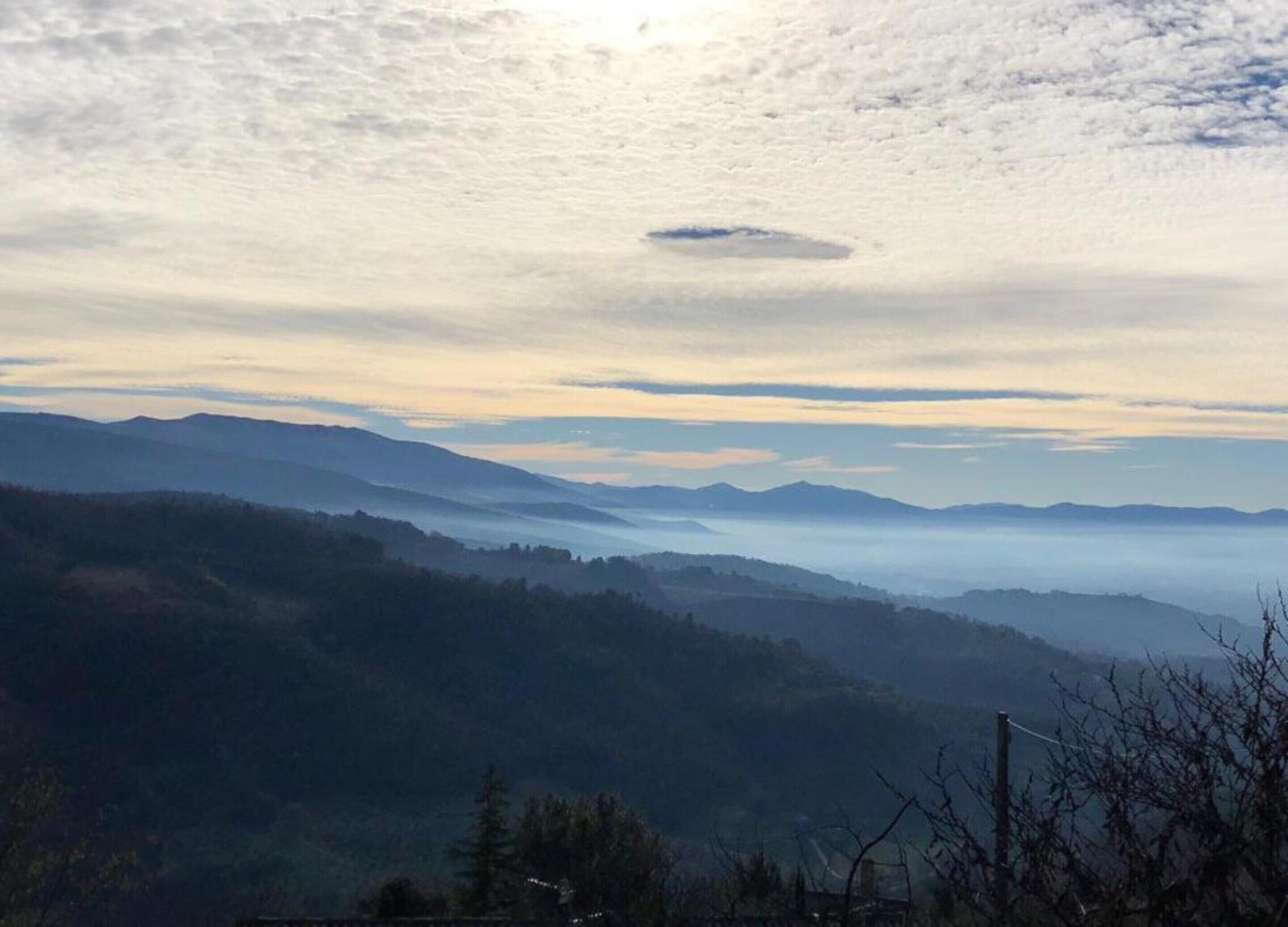 A mountainous landscape with a clear sky and a sun partially obscured by clouds.