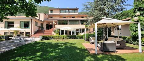 Ein modernes, zweistöckiges Gebäude mit einer Terrassenfläche, Außenmöbeln und einem Pool.