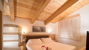 A bedroom with a wooden ceiling, a bed with white linens, a nightstand, a wall-mounted TV, and a stone fireplace. - Apartment in Umbria With Pool and Sauna (Foligno)