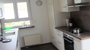 A compact kitchen with white cabinets, a stove, a sink, and a window with a view of greenery. - Forgetful the big one (Titisee-Neustadt)