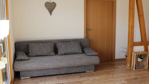 A grey sofa with cushions, a wooden door, and a heart-shaped decoration on the wall. - Forgetful the big one (Titisee-Neustadt)