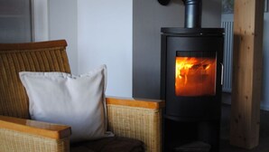 A room with a wicker chair, a white pillow, and a wood-burning stove.