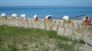 A beach with white beach chairs and a striped beach umbrella. - Haus Kranich Modern Retreat (Glowe)