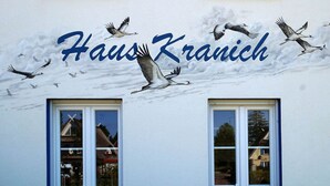 A building facade with the name "Haus Kranich" and a mural of birds flying. - Haus Kranich Modern Retreat (Glowe)